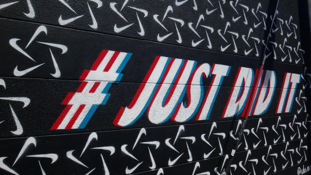Nike mural reading #JUSTDIDIT on a wall covered in swoosh logos